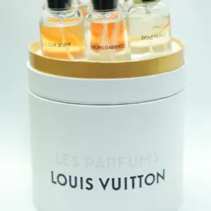 Estuche cilíndrico blanco y dorado de perfumes Louis Vuitton, que contiene varios frascos miniatura de vidrio con tapa negra y etiquetas visibles.